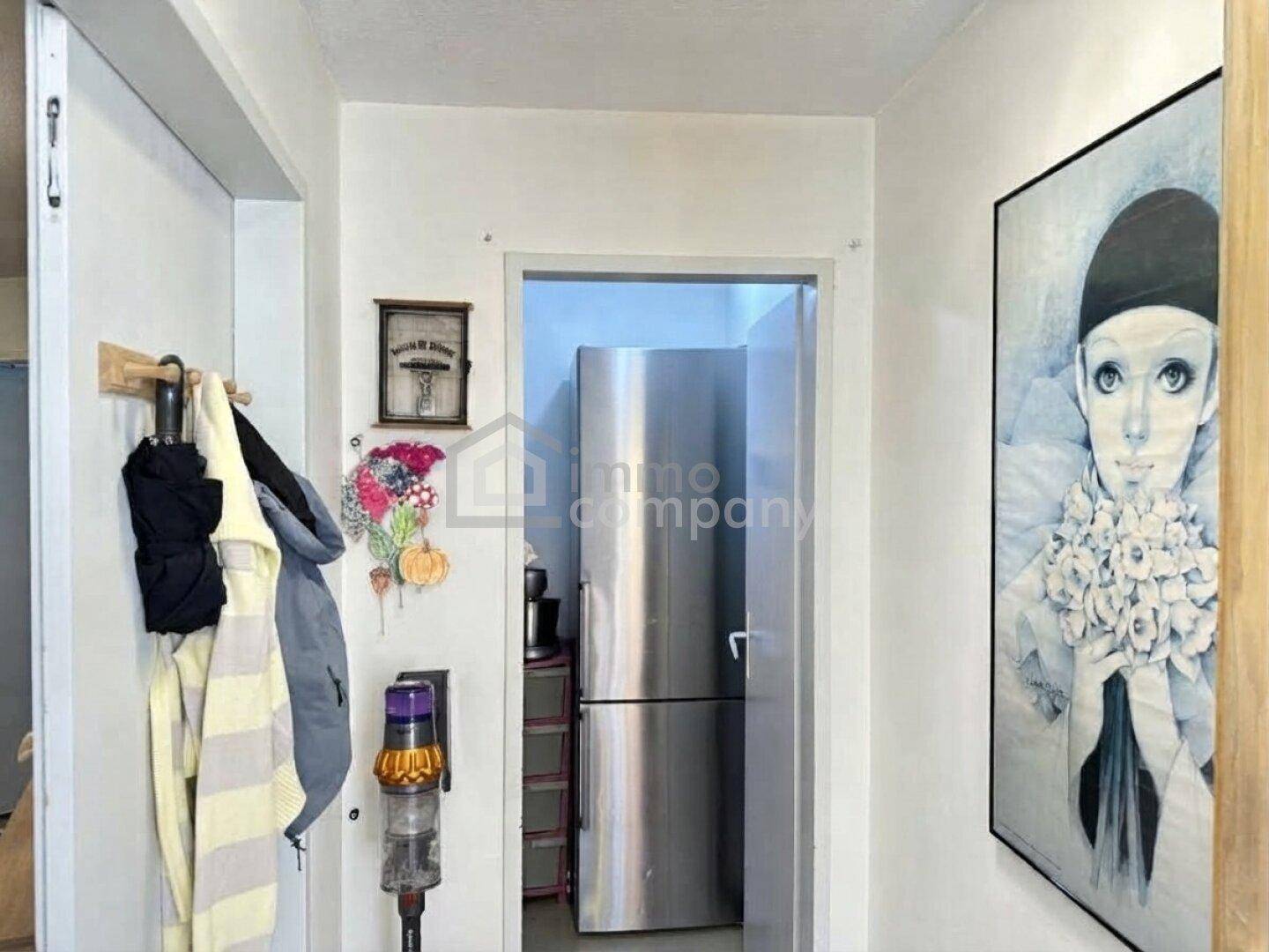 Eingangsbereich mit Garderobe, Kunstwerk und Blick auf einen modernen Kühlschrank.