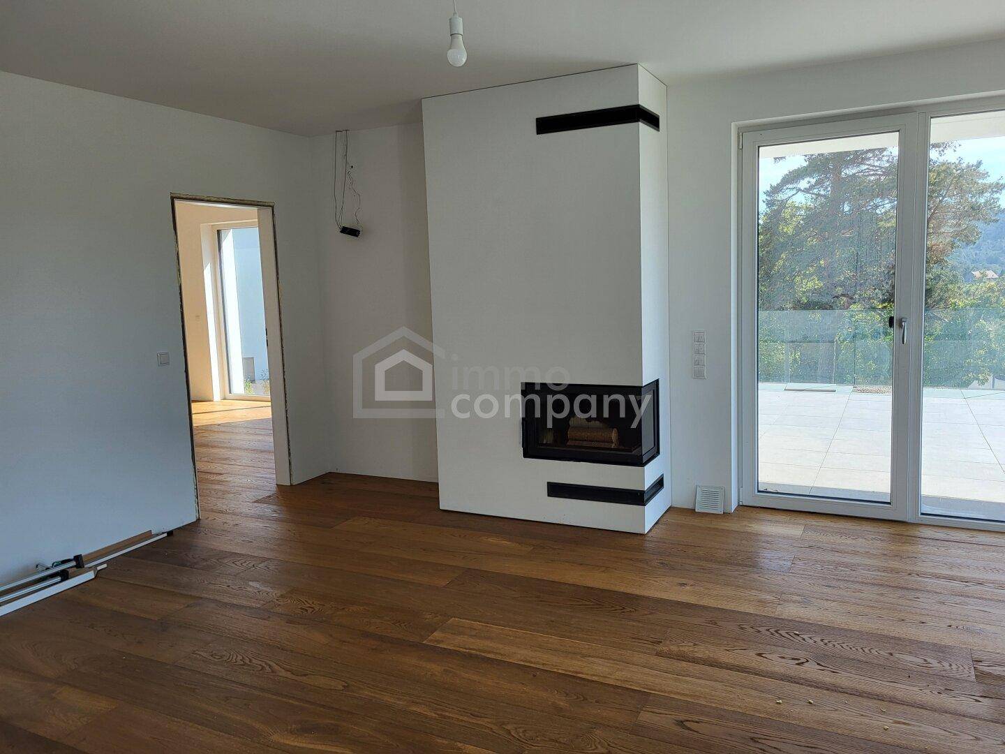 Lichtdurchfluteter Wohnbereich mit modernem Kamin, Holzboden und großem Terrassenzugang.