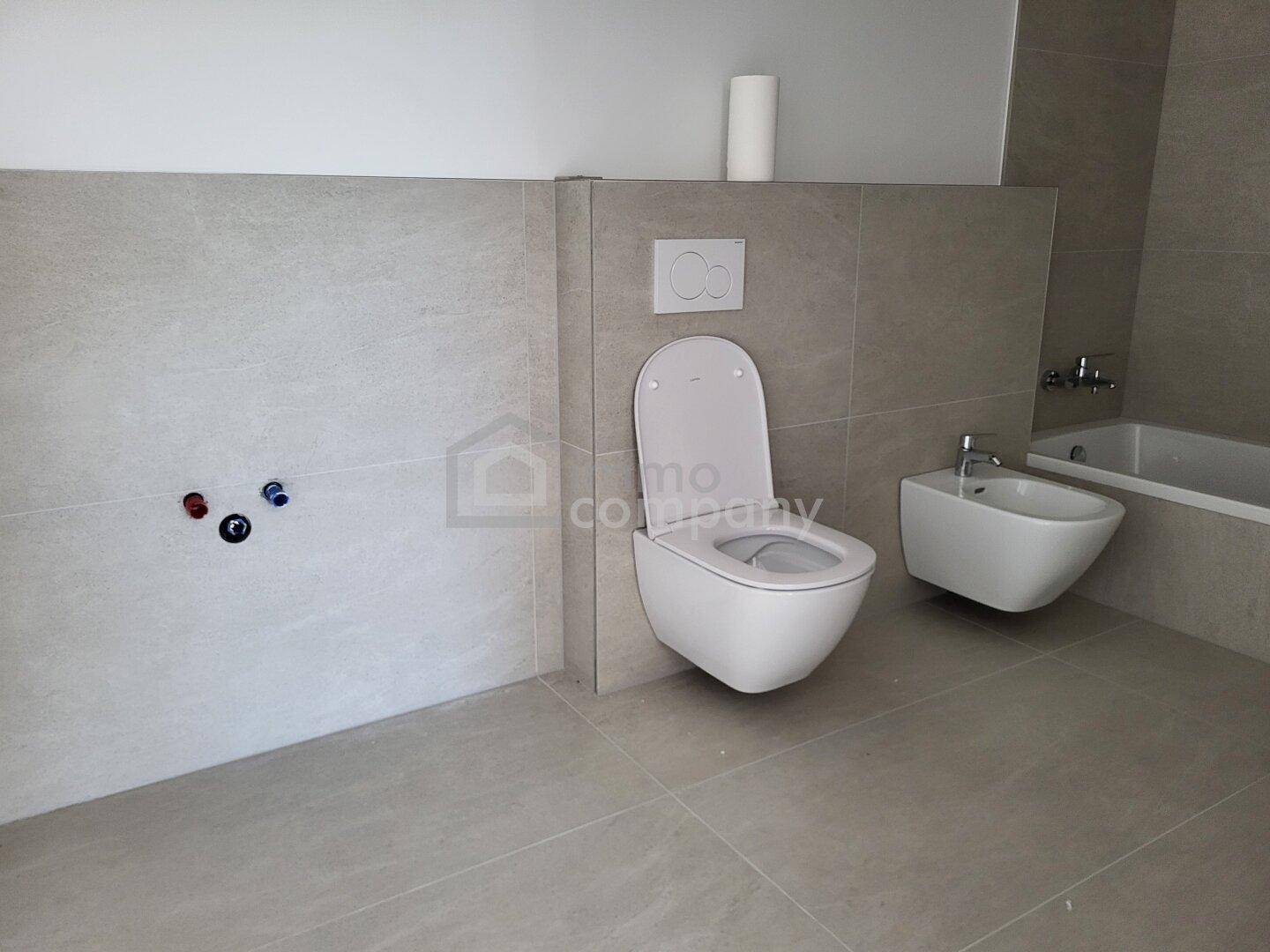 Modernes Badezimmer mit Wand-WC, Bidet und Badewanne in hellen Fliesenfarben.