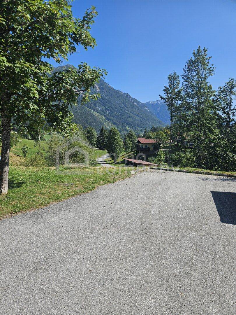 Serpentinenstraße führt durch eine grüne Hügellandschaft mit einem Haus im Hintergrund und Bergblick.