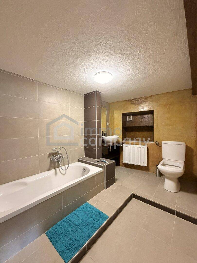 Modernes Badezimmer mit Badewanne, WC und Waschbecken, ausgestattet mit beigen Fliesen.
