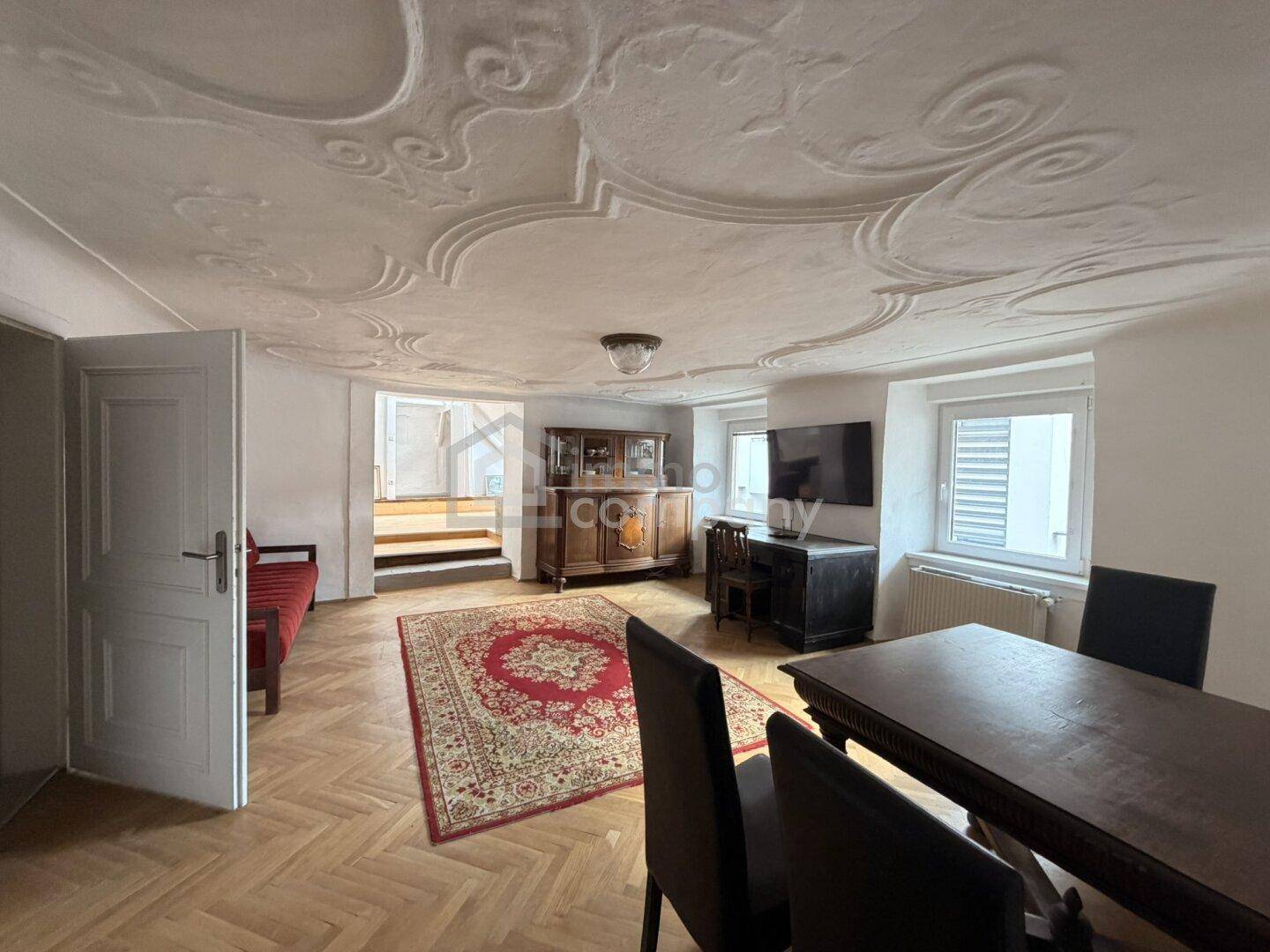 Wohn- und Essbereich mit kunstvoller Stuckdecke, Fischgrätparkett und traditionellen Möbeln.