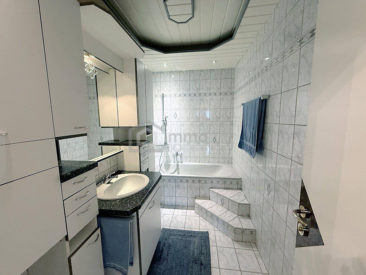 Gefliestes Badezimmer mit Badewanne, Waschbecken und praktischem Stauraum für Utensilien.