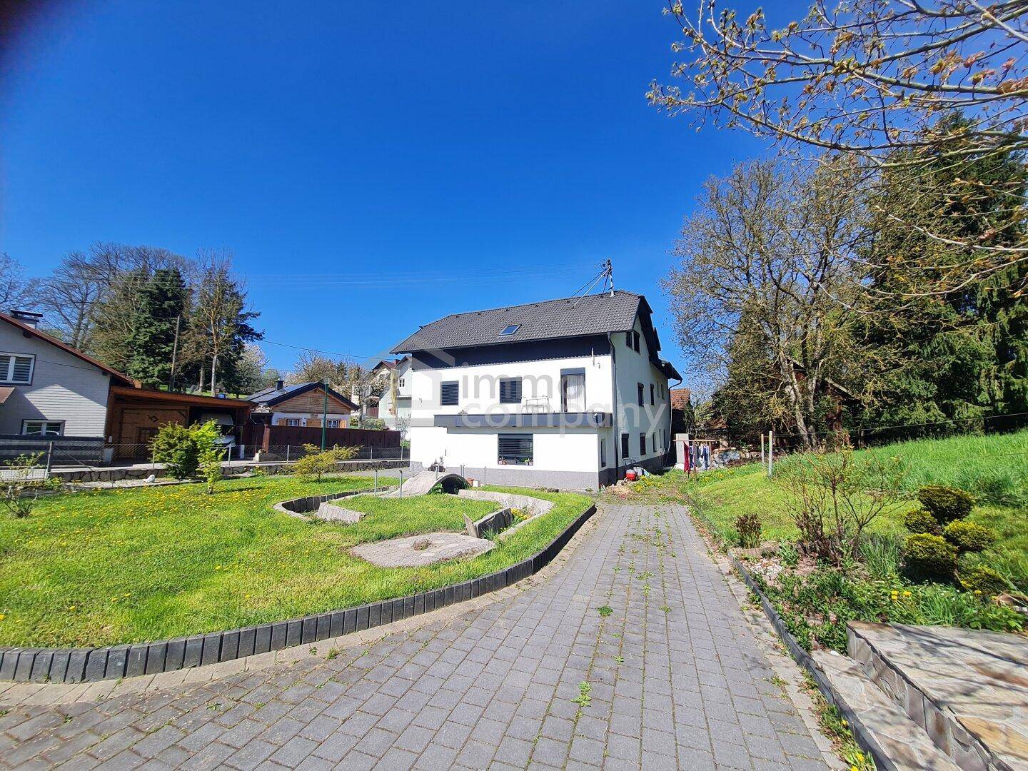 Außenansicht eines Einfamilienhauses mit gepflasterter Auffahrt und Gartenbereich unter blauem Himmel.