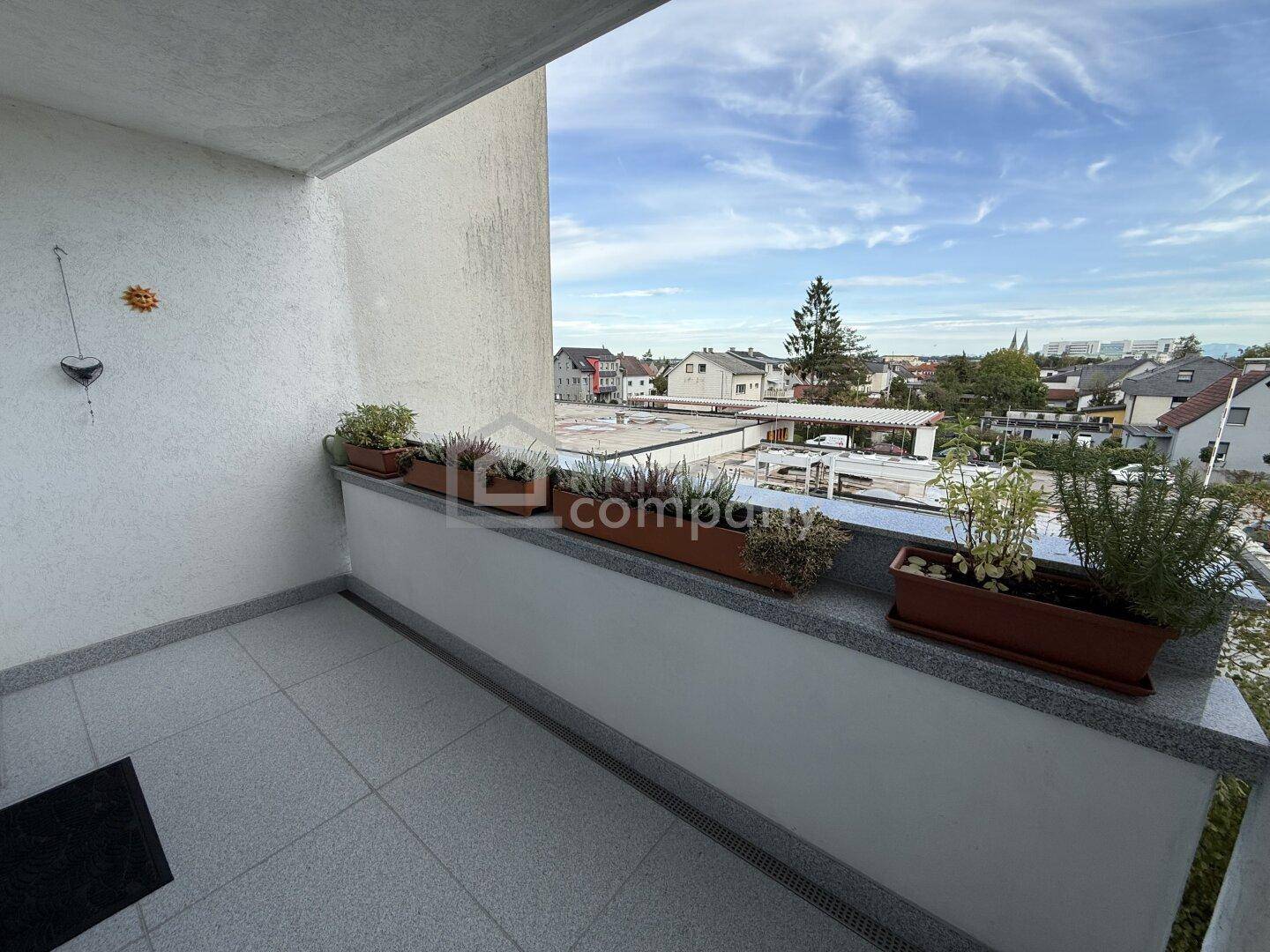 Balkon mit Fliesenboden, Blumenkästen und weitem Blick über die Dächer der Stadt.