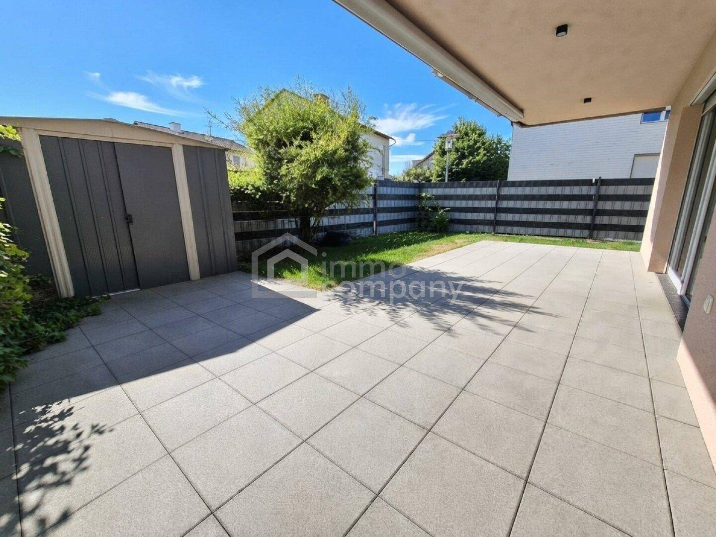 Sonnige Terrasse mit großzügiger Pflasterfläche, angrenzendem Garten und Geräteschuppen.