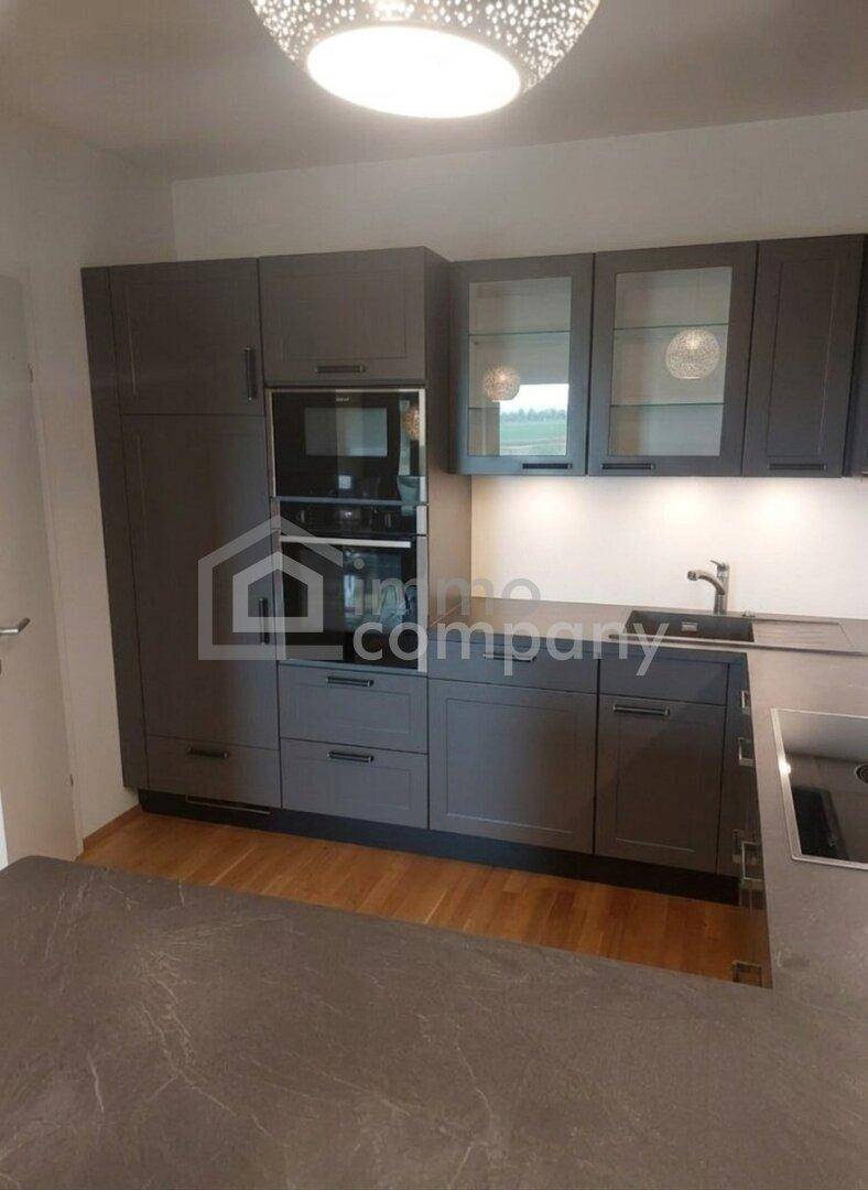 Moderne Küche mit grauen Schränken, integriertem Backofen und Holzboden, funktional und stilvoll.