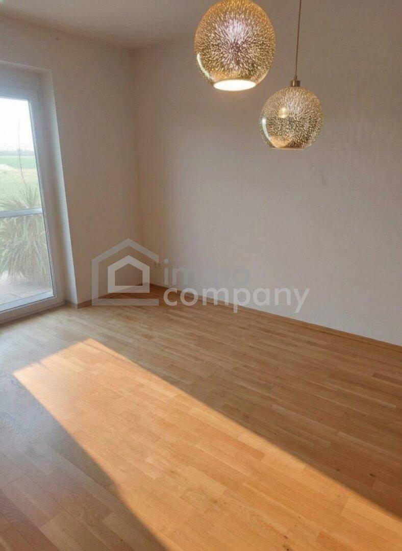 Heller Raum mit Holzboden, großem Fenster und dekorativen Hängelampen, durchflutet von Sonnenlicht.