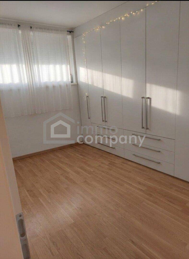 Schlafzimmer mit weißen Einbauschränken, hellem Holzboden und Fenster mit Vorhängen, bietet praktischen Stauraum.