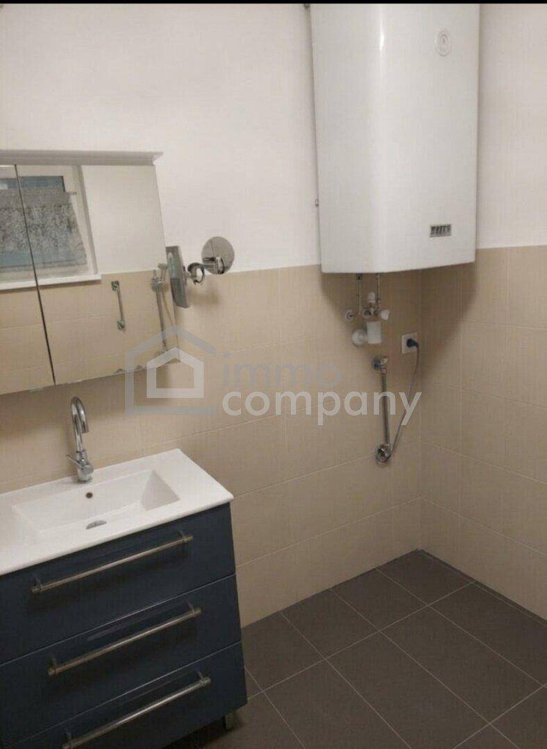 Badezimmer mit Einzelwaschbecken, Spiegelschrank und Warmwasserboiler, funktional und hell gefliest.