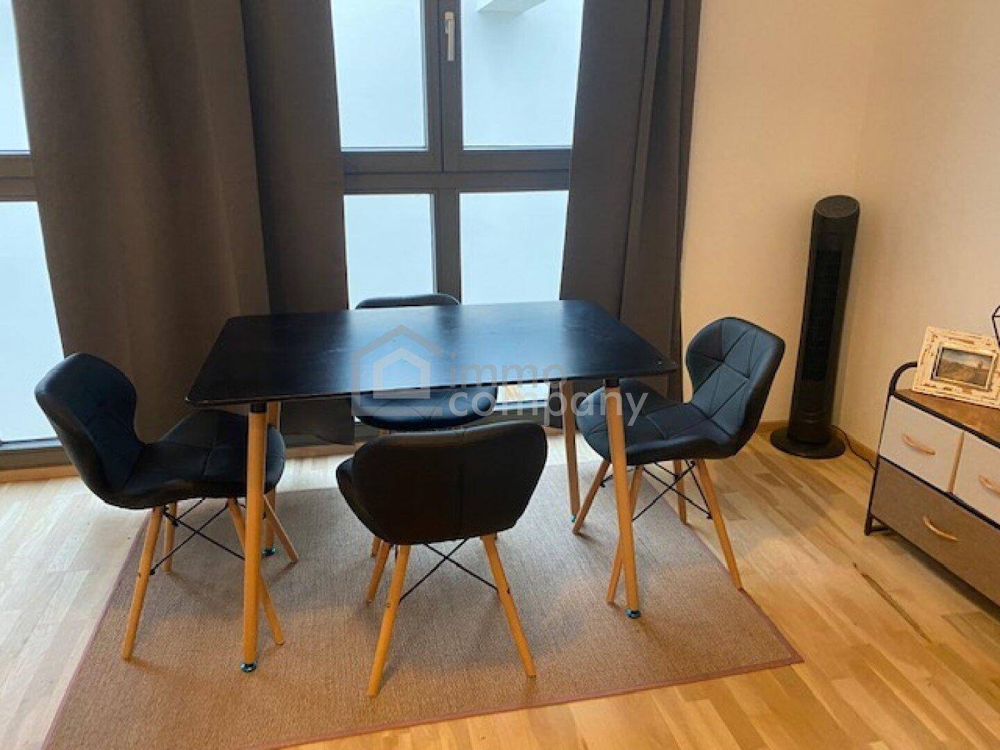 Essbereich mit modernem schwarzem Tisch und Stühlen vor großen Fenstern mit dunklen Vorhängen.