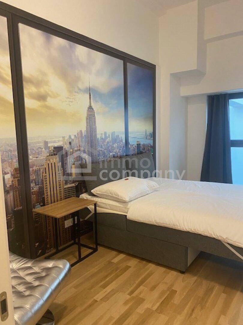 Schlafzimmer mit Bett, Nachttisch und einer großen Wandtapete mit Stadtansicht.