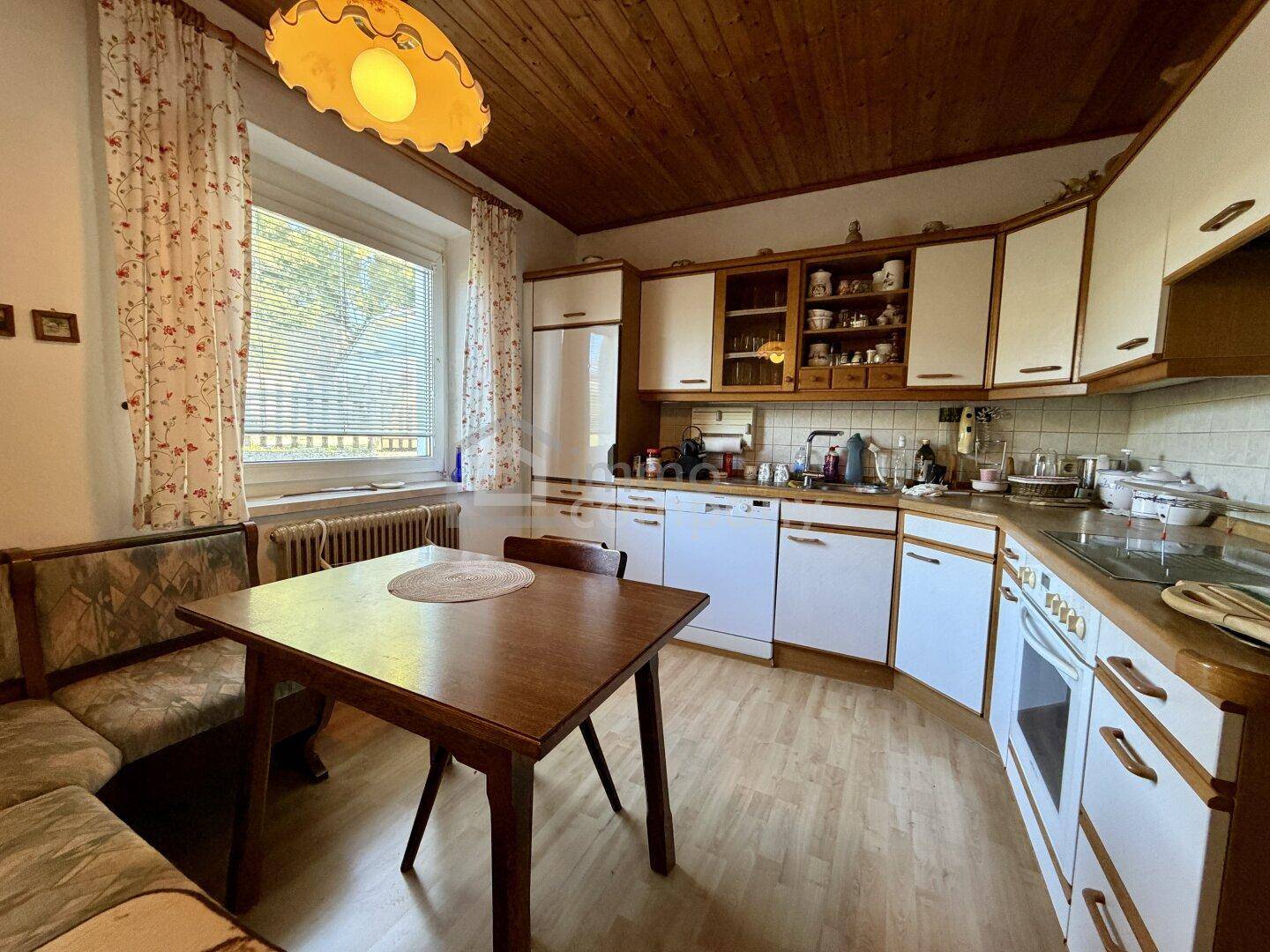 Traditionelle Wohnküche mit integriertem Essbereich, Holzdecke und hellen Schränken. Ein Fenster sorgt für natürliches Licht.
