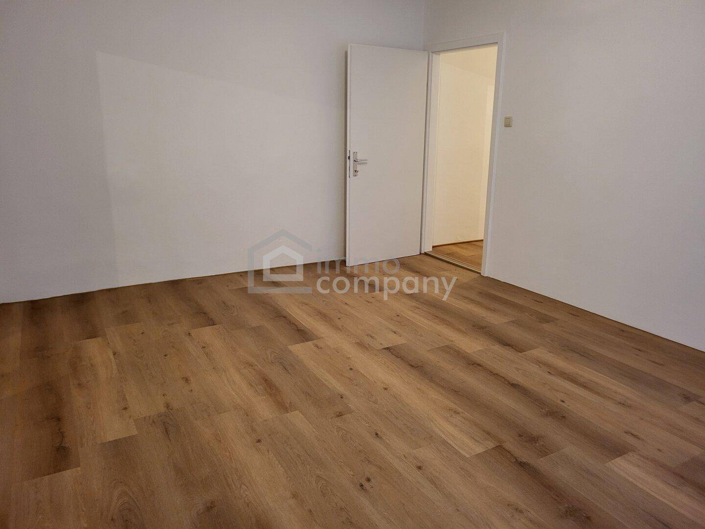 Leeres Zimmer mit Laminatboden und offener Tür, bereit zur individuellen Gestaltung.