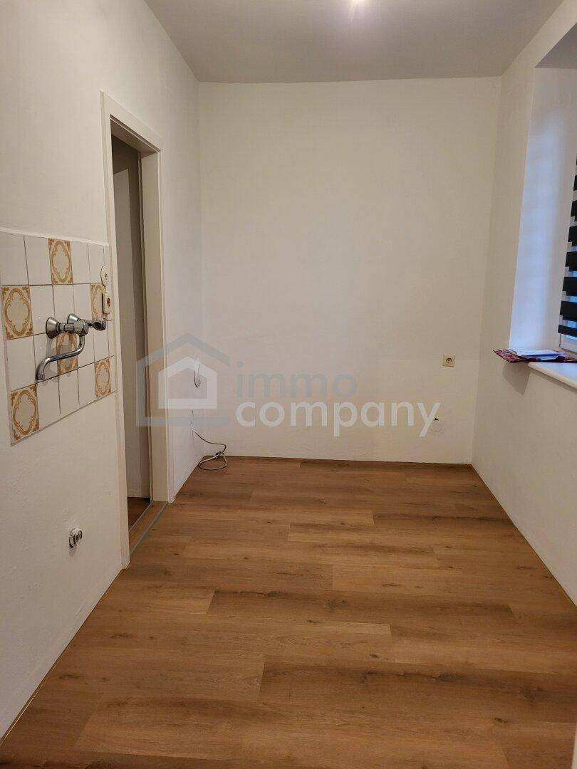 Raum mit Laminatboden, Fenster und gefliestem Bereich mit Wasseranschlüssen.