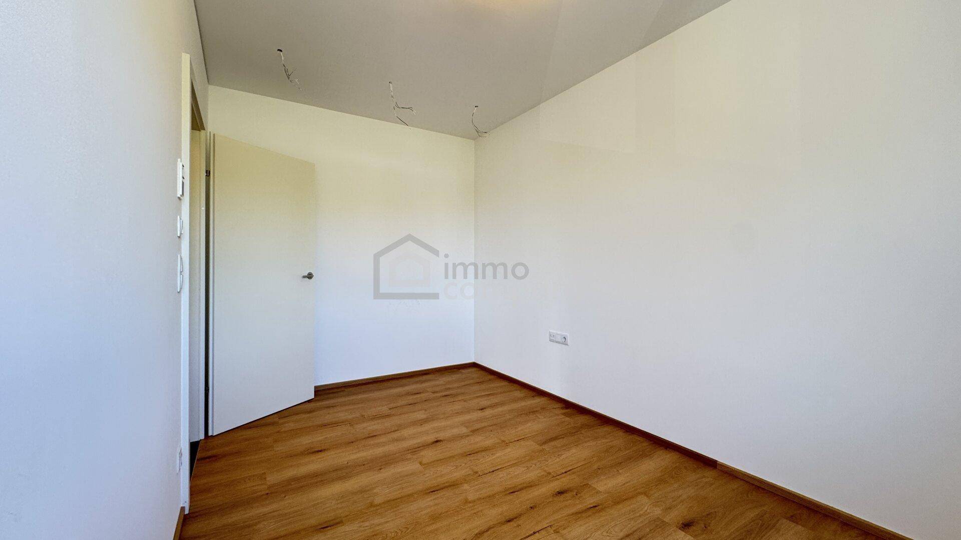 Leeres Zimmer mit Laminatboden und weißen Wänden, ideal als Schlaf- oder Arbeitszimmer.