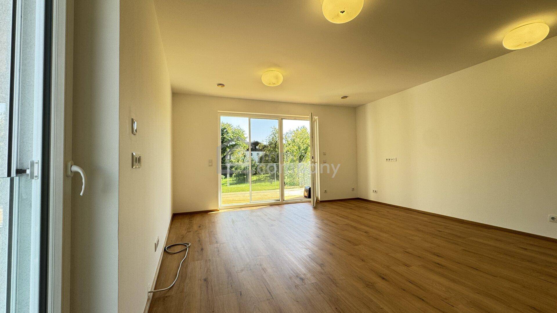Geräumiges, leeres Wohnzimmer mit Laminatboden und großer Schiebetür zum Gartenbereich.