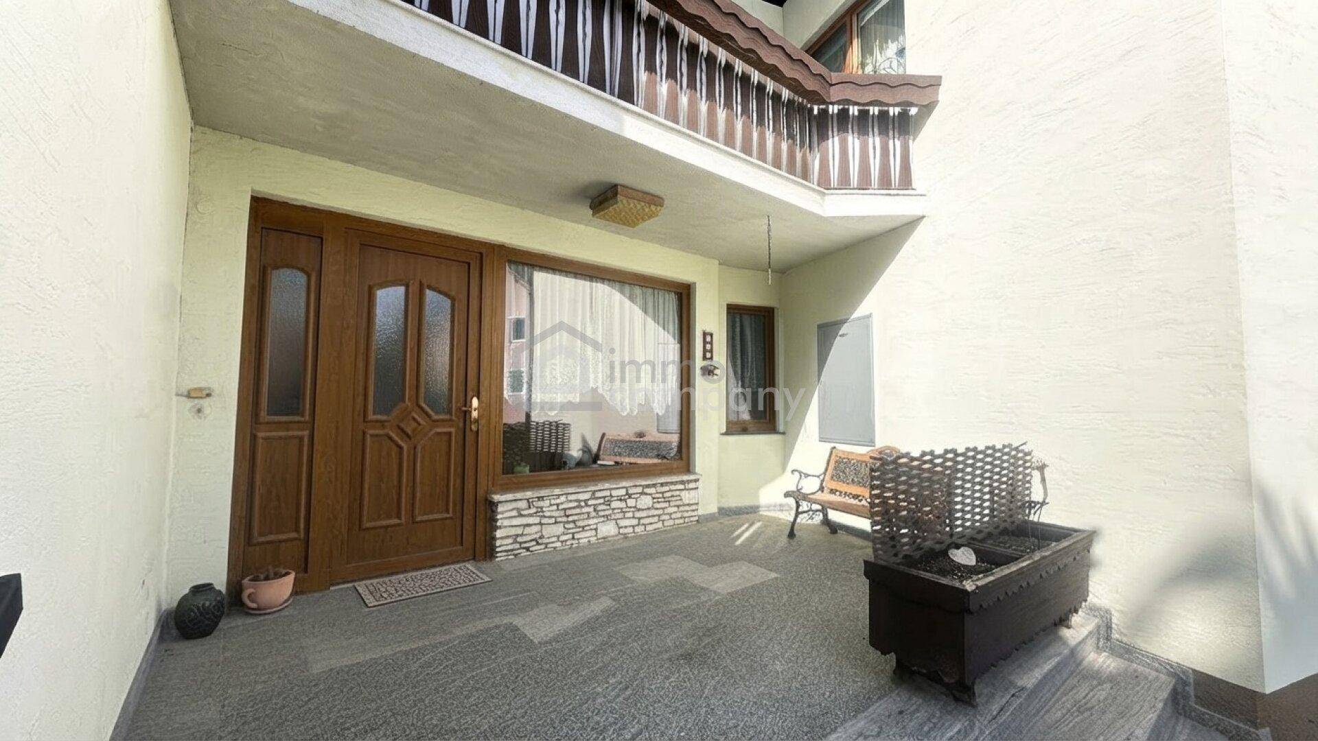 Eingangsbereich des Hauses mit Holztür und kleiner überdachter Veranda, umgeben von Steinakzenten.