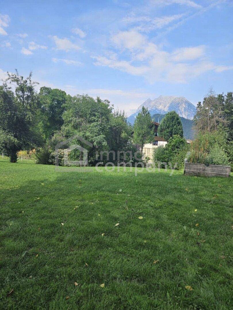 Weitläufige Rasenfläche eines Gartens mit Bäumen und beeindruckendem Bergblick.