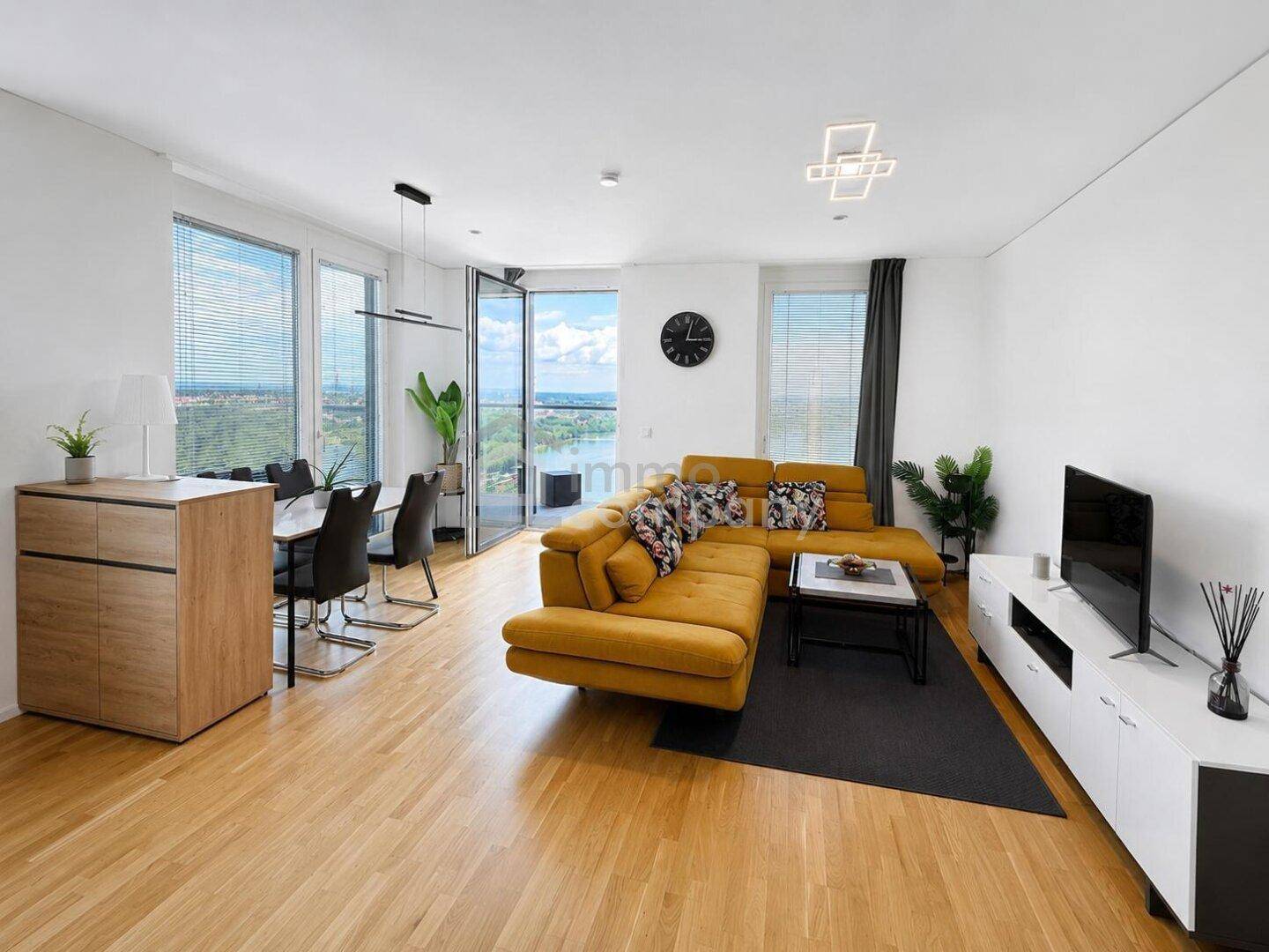 Geräumiger, heller Wohn- und Essbereich mit modernem Sofa und Blick auf die Stadt und den Fluss.
