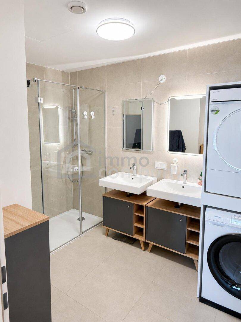Modernes Badezimmer mit begehbarer Dusche, Doppelwaschbecken und integrierter Waschmaschine und Trockner.