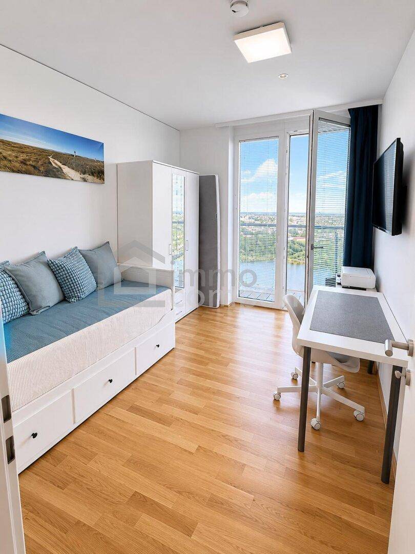 Freundliches Schlafzimmer mit Tagesbett, Schreibtisch und Zugang zum Balkon mit weitem Flussblick.