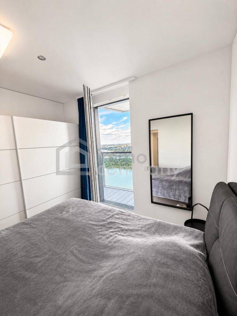 Helles Schlafzimmer mit großem Bett, weißem Kleiderschrank und Zugang zum Balkon mit Flussblick.