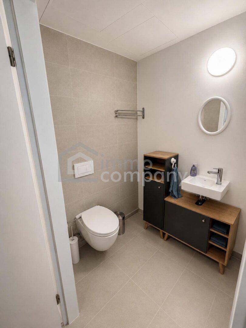 Modernes Gäste-WC mit wandhängender Toilette, kleinem Waschbecken und hellen Fliesen.