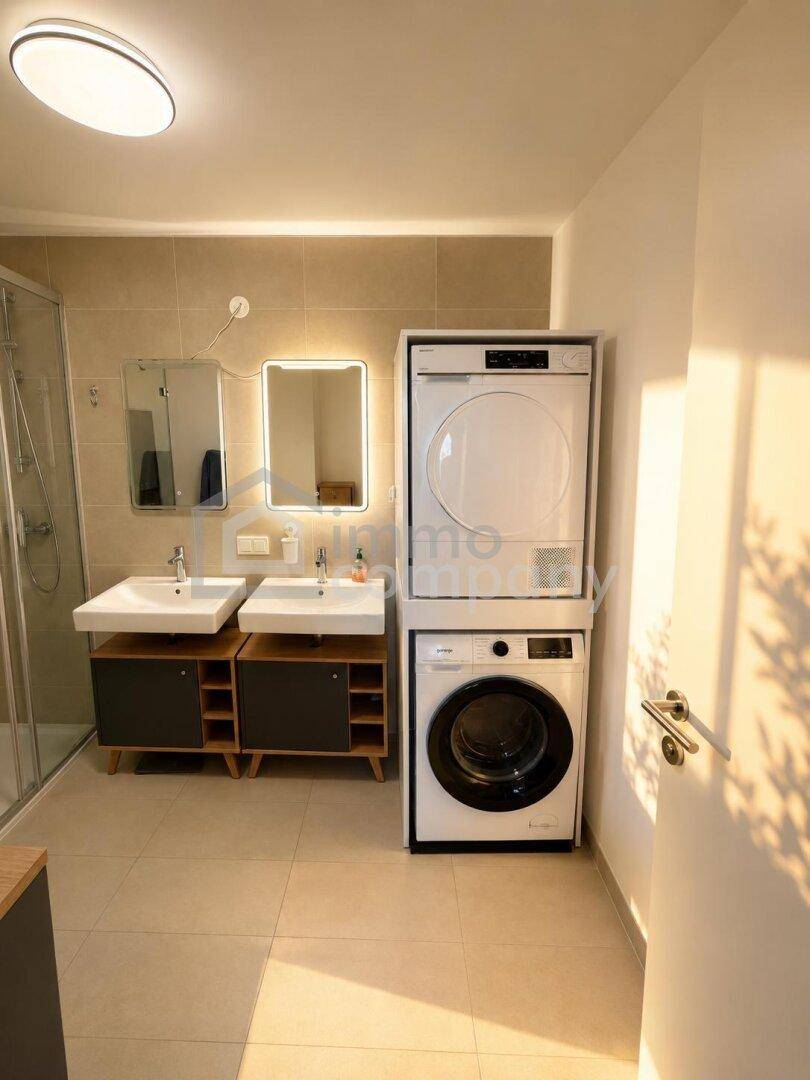 Helles Badezimmer mit Doppelwaschbecken, moderner Dusche und praktischer Wasch-Trocken-Säule.