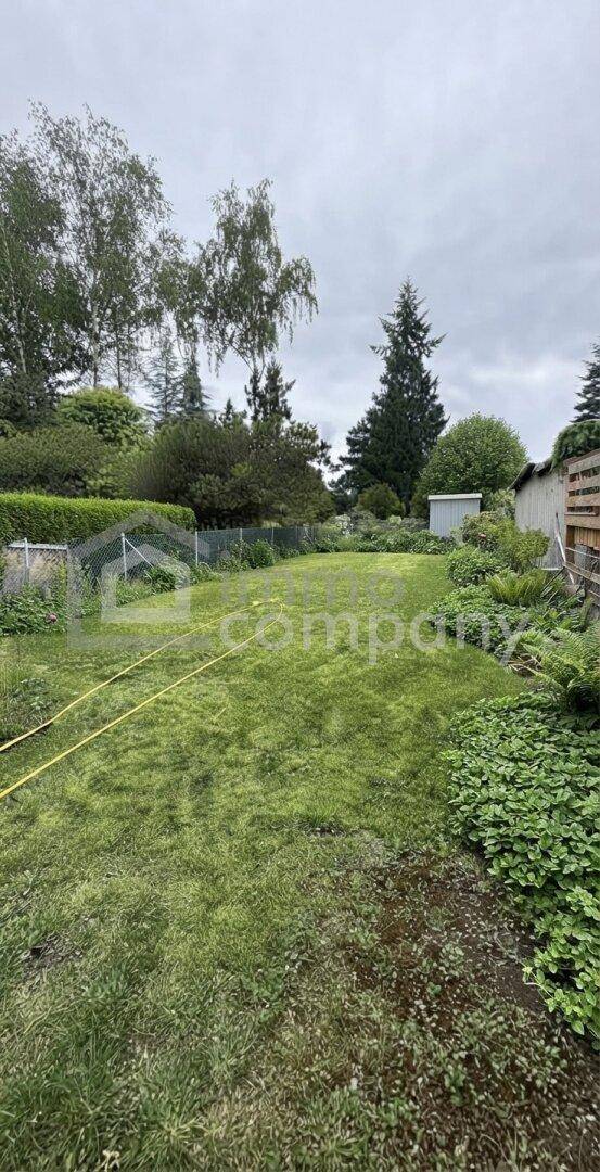 Großer, gepflegter Garten mit weitläufiger Rasenfläche und hohen Bäumen im Hintergrund.