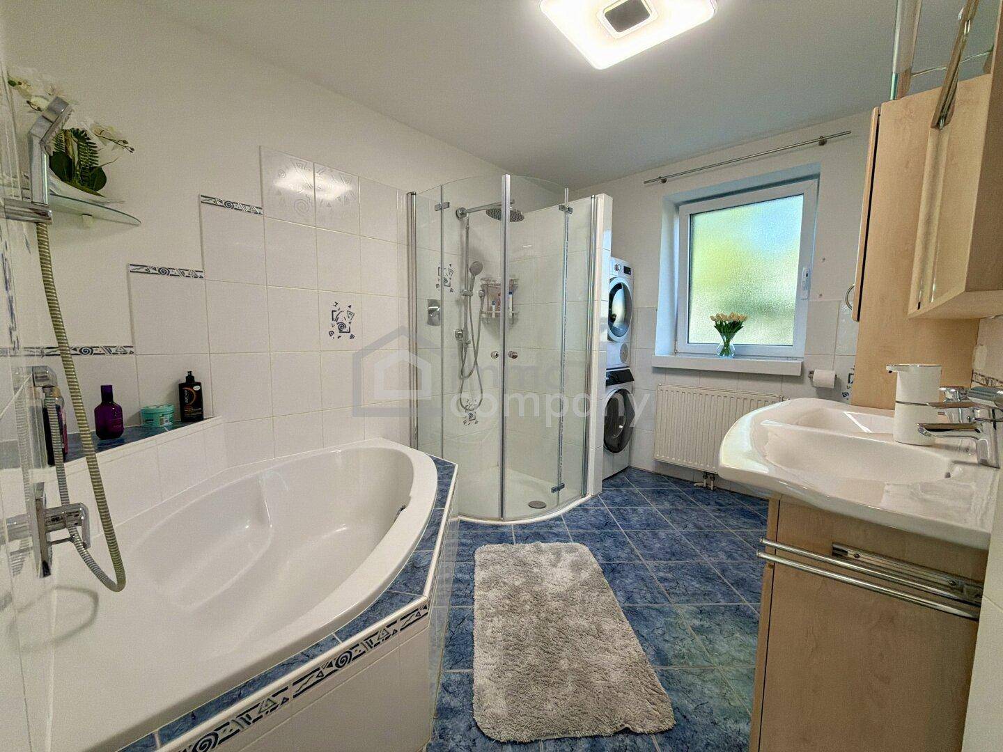 Badezimmer mit Badewanne, Dusche, Doppelwaschbecken und Waschmaschine.
