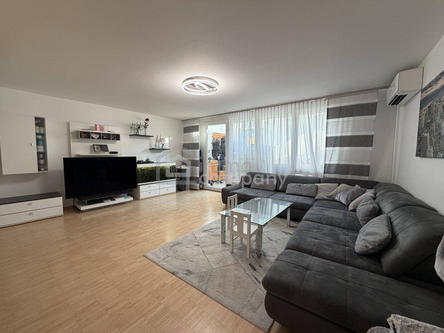 Geräumiges Wohnzimmer mit großem Ecksofa, Holzboden und Zugang zu einem Außenbereich.