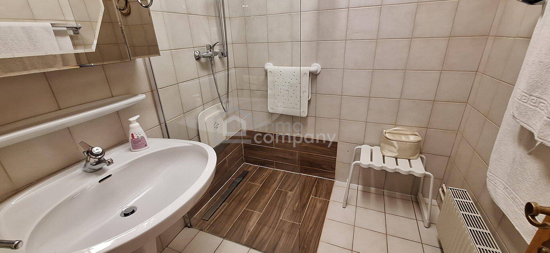 Modernisiertes Badezimmer mit ebenerdiger Dusche, Waschbecken und Heizkörper.
