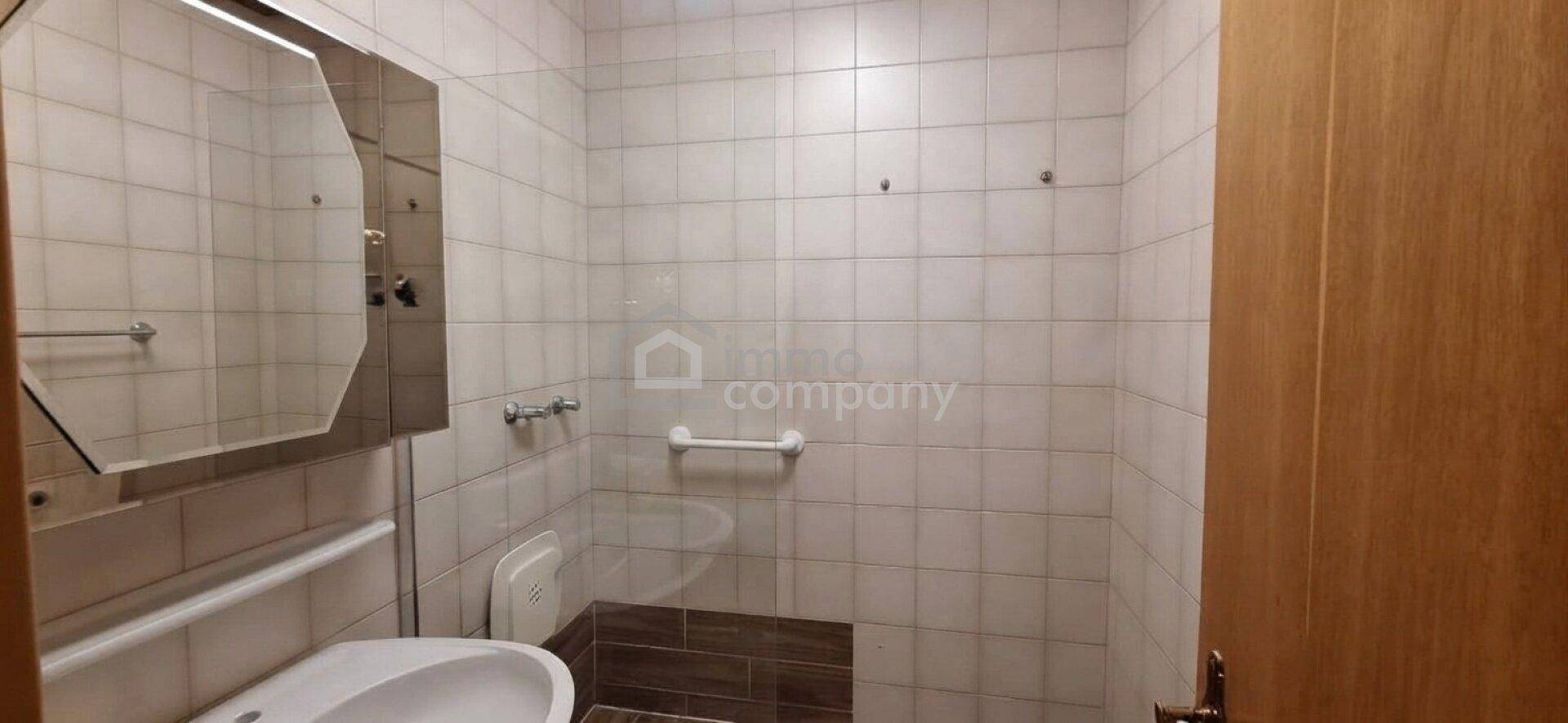 Badezimmer mit hellen Fliesen, Spiegelschrank und einer Haltestange für zusätzliche Sicherheit.