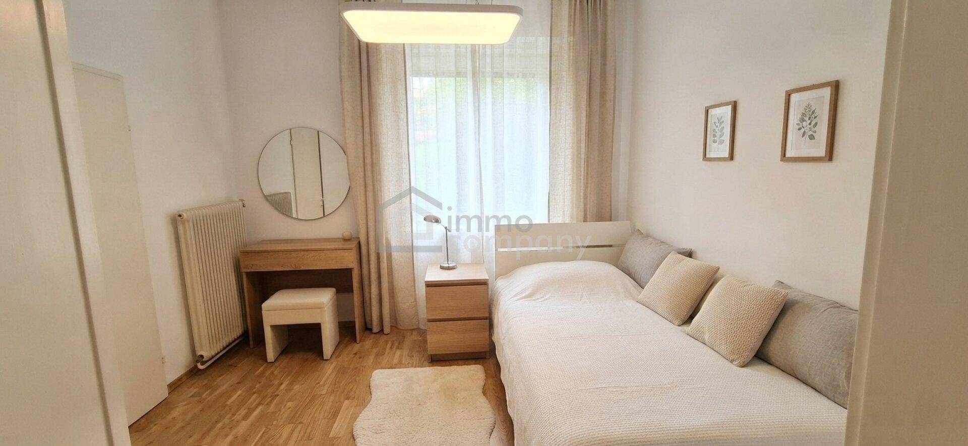 Helles Schlafzimmer mit Einzelbett, Holzboden und einem Schminktisch am Fenster.