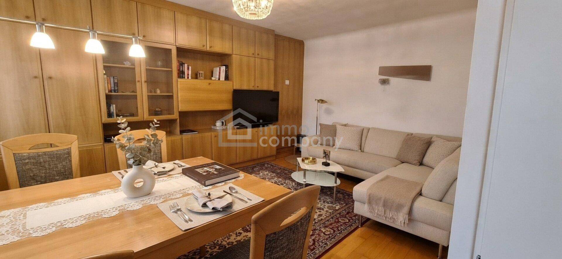 Heller Wohn- und Essbereich mit Holzmöbeln, beigem Sofa und einem großen Esstisch.