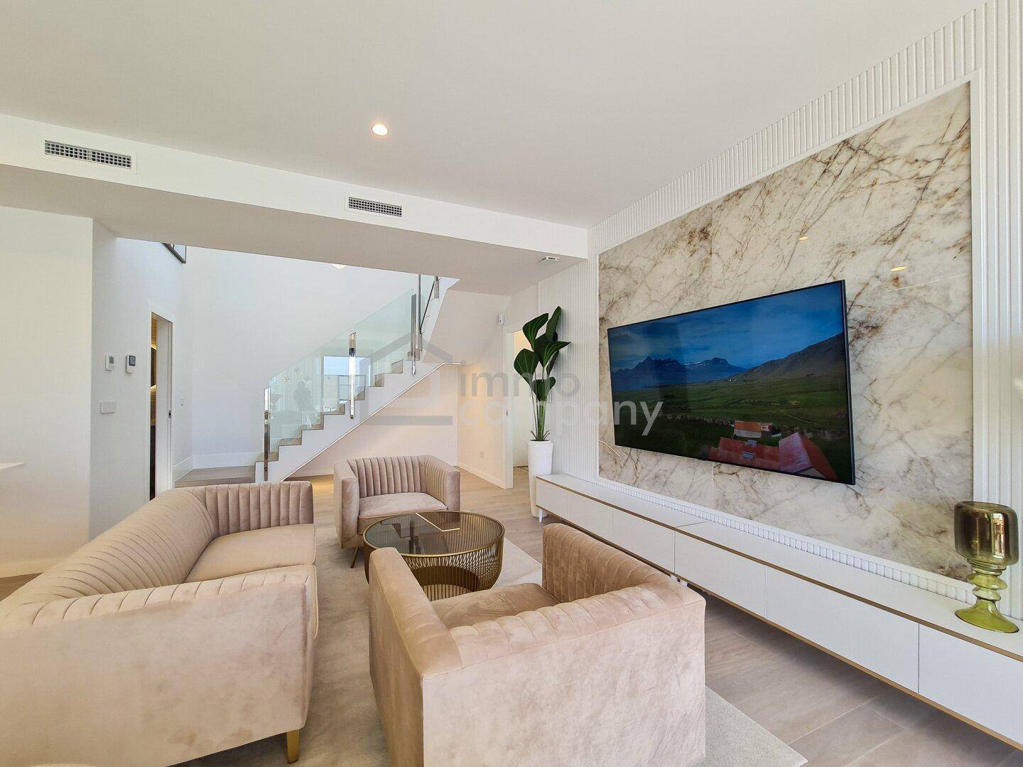 Elegantes Wohnzimmer mit Marmorwand, großem Fernseher und offener Treppe im Hintergrund.