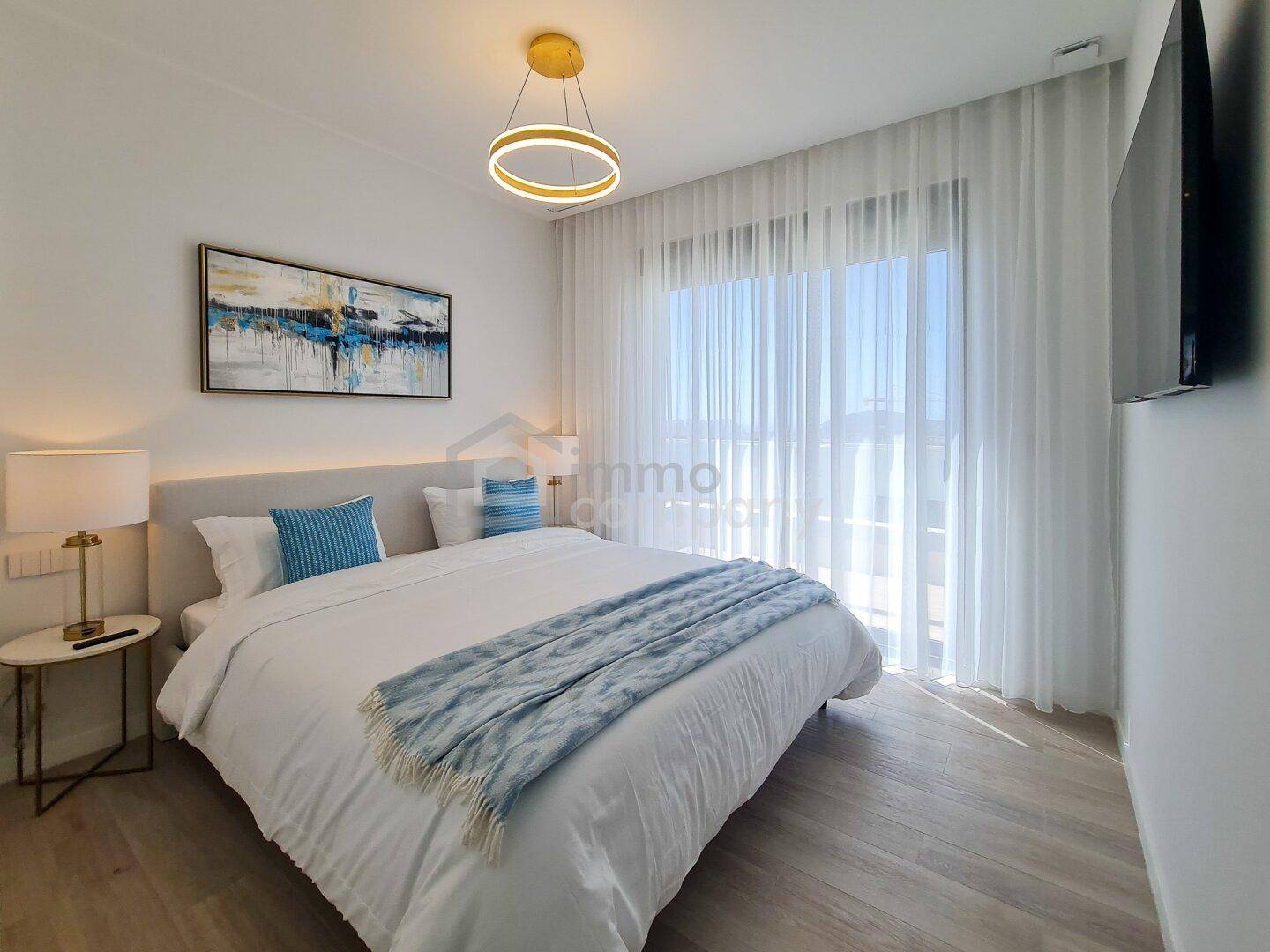 Helles Schlafzimmer mit großem Bett, moderner Einrichtung und bodentiefen Fenstern.