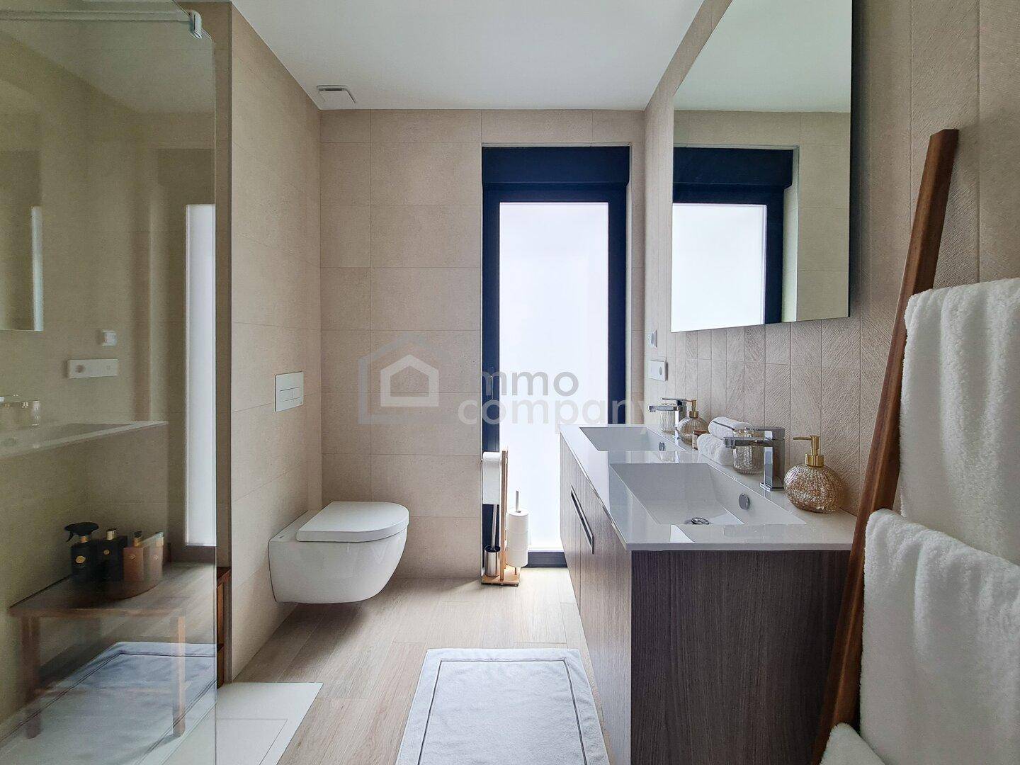 Modernes Badezimmer mit Doppelwaschbecken, wandhängendem WC und großer begehbarer Dusche.