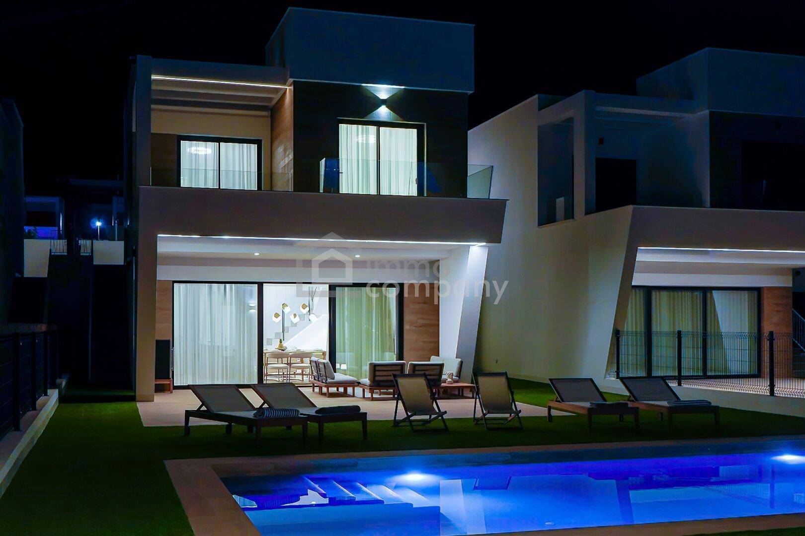 Beeindruckende Außenansicht der modernen Villen bei Nacht mit beleuchtetem Pool und Terrasse.
