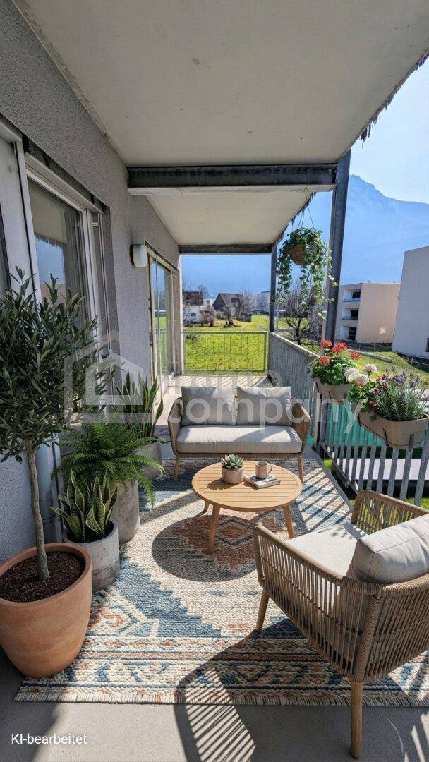 Möblierter Balkon mit bequemen Sitzgelegenheiten, Pflanzen und einem weiten Blick auf grüne Felder und Berge.