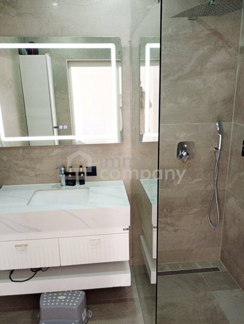 Modernes Badezimmer mit begehbarer Dusche, beleuchtetem Spiegel und Einzelwaschbecken.