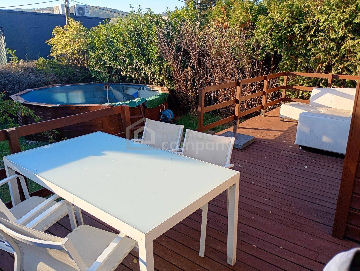 Holzterrasse mit Esstisch und Lounge-Bereich, angrenzend an einen Aufstellpool im Garten.