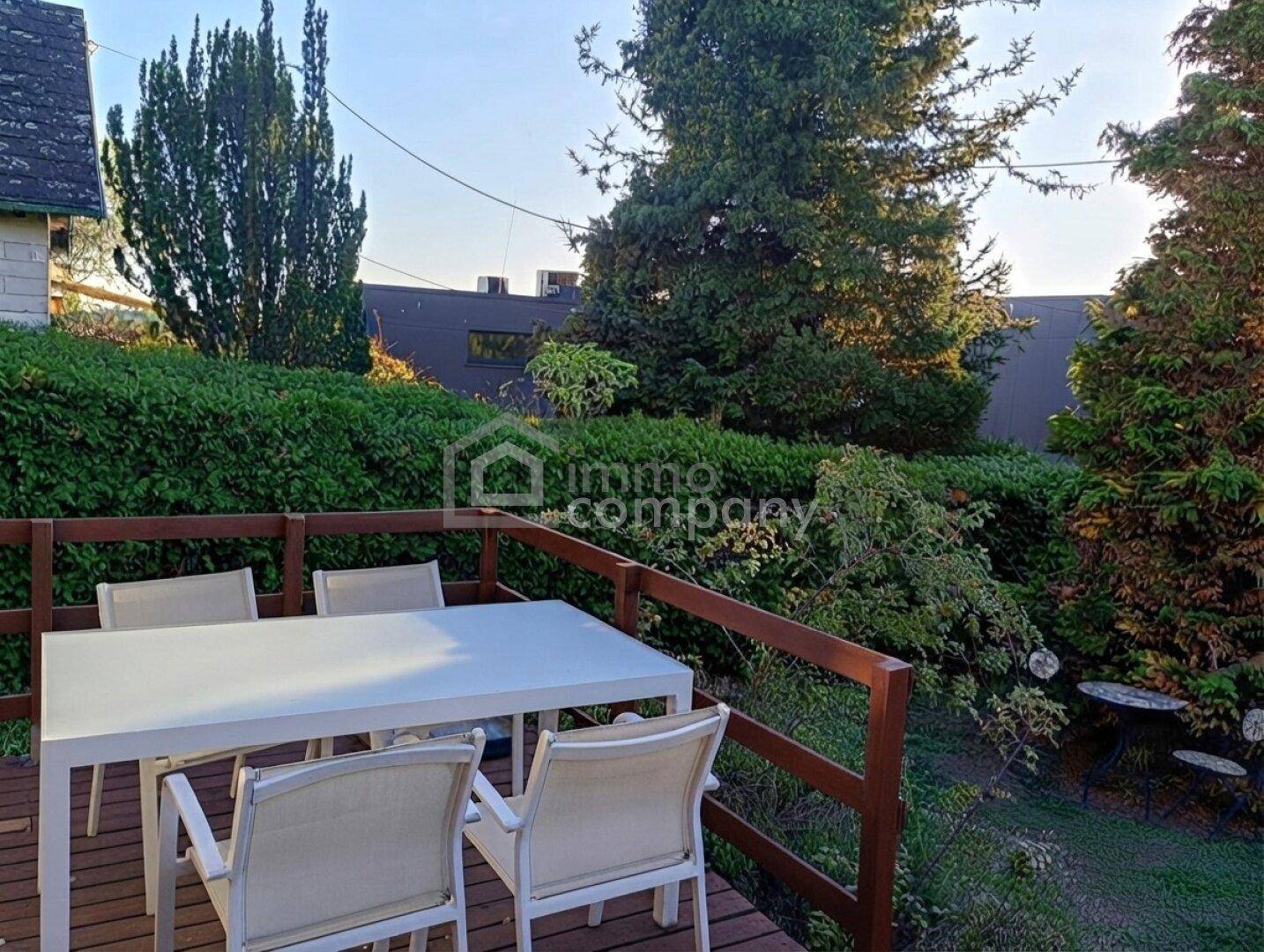 Geräumige Holzterrasse mit Essbereich und Blick auf die umgebende grüne Bepflanzung.