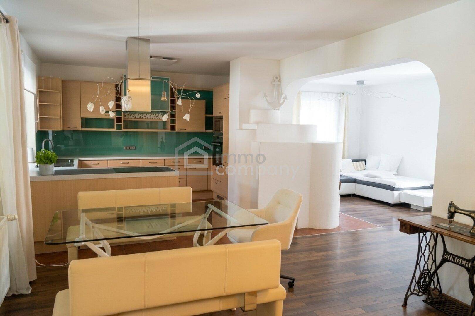 Moderne Einbauküche mit Essbereich, Holzfronten, grüner Rückwand und offenem Übergang zum Wohnbereich.