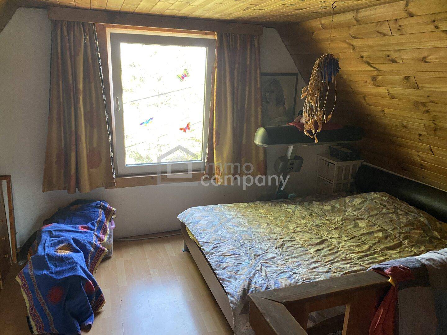 Schlafzimmer mit Holzwänden, Dachschräge und Fenster mit Blick ins Grüne und Laminatboden.