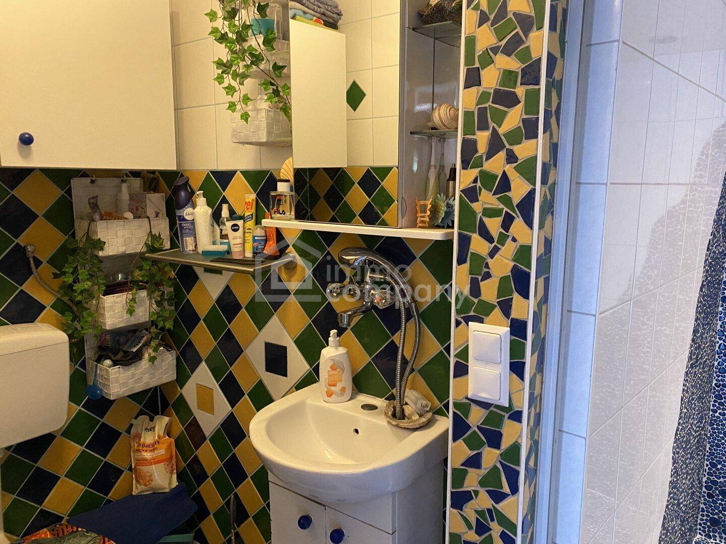 Badezimmer mit farbenfrohen Fliesen, kleinem Waschbecken und Spiegelschrank über dem Waschtisch.