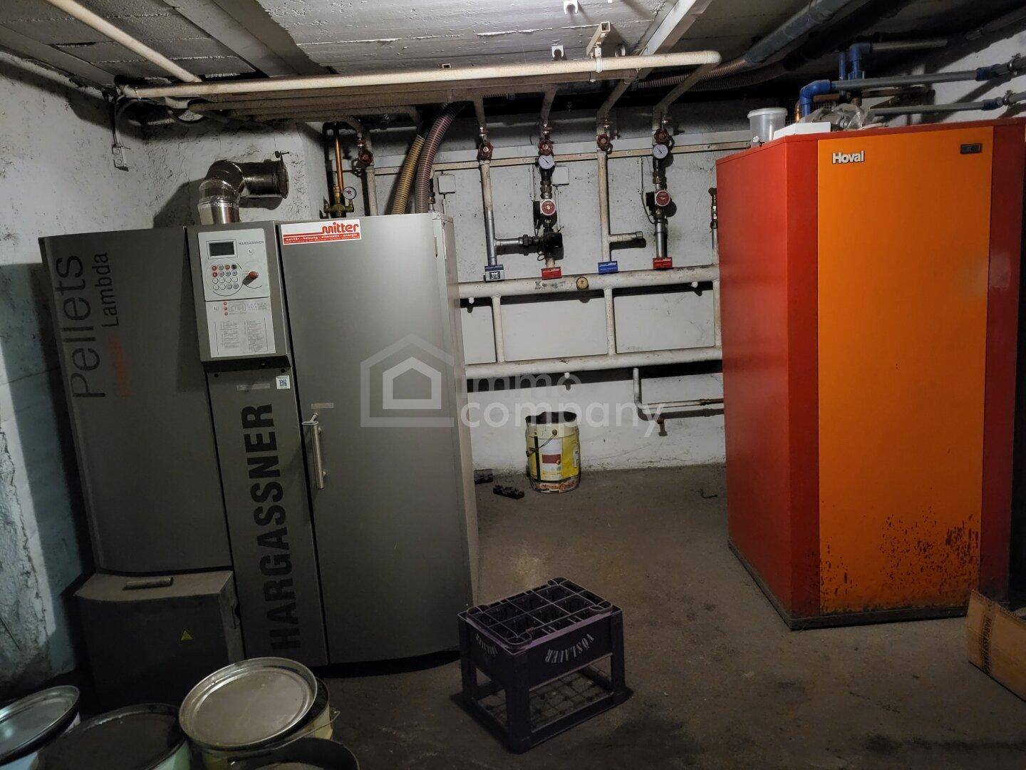 Heizungsraum mit Pelletsheizung und Warmwasserspeicher, sowie sichtbaren Rohren und Installationen.