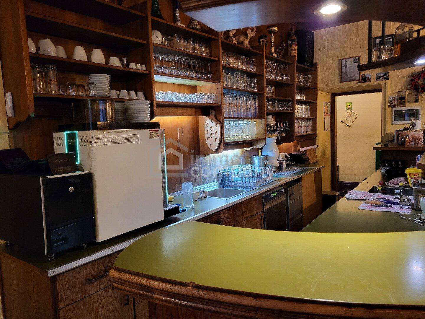 Bar- und Küchenbereich mit Holzregalen, Spüle und professionellen Geräten, bereit für den Betrieb.