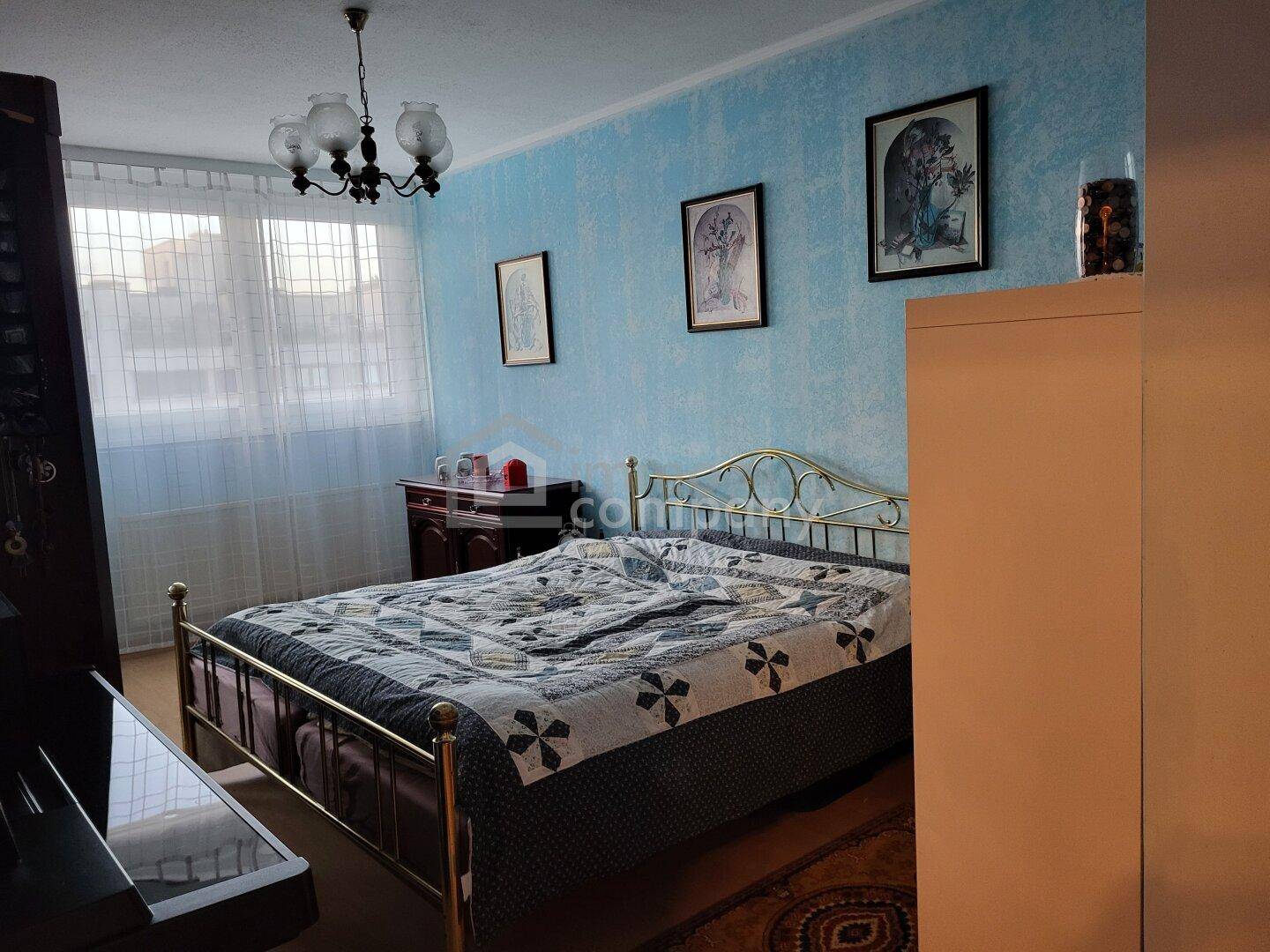 Schlafzimmer mit blau gestrichenen Wänden, Metallbett und einem Fenster mit hellen Vorhängen.